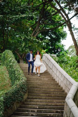 Interracial aşıklar çifti parkta taş merdivenlerden gün boyunca çalıştırın. Bir Hintli Çinli bir kadını evleniyor ve onlar zevk ve neşe içinde merdivenlerden aşağı çalışan.