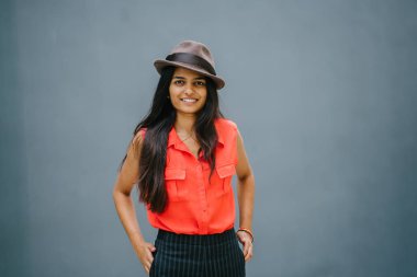 Bir genç, çekici Hint Asya portresi öğrenci moda. O gülümseyen ve güneşin düz gri mavi arka plan karşı ayakta.