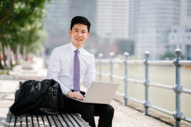 Singapur Nehri boyunca onun dolma kalem ile bir dizüstü dizüstü bilgisayar ile gün içinde yazılı Asya adam portresi. O profesyonel bir beyaz gömlek giymiş, ama onun ceket kravat vardır.