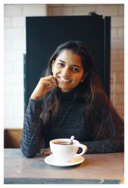 Sıcak bir kahve keyfi bir kafeterya masada oturan bir genç çekici Hint Asyalı kadın portresi. O raslantı giyimli ve konforlu, rahat ve mutlu görünüyor.