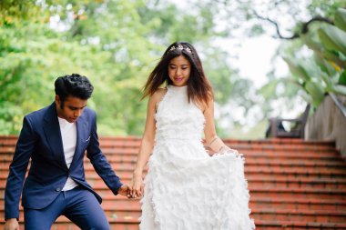 Interracial aşıklar çifti parkta taş merdivenlerden gün boyunca çalıştırın. Bir Hintli bir Çinli kadın zevk ve neşe içinde evleniyor.