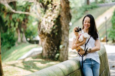 Pet shih tzuh köpeğini gün yeşilliklerle dolu bir parkta ve bitkiler içinde belgili tanımlık geçmiş olan bir genç, çekici ve güzel pan Asya kadın portresi.