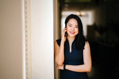 Onun smartphone bir pencere günde kullanan bir genç ve çekici Çinli Asyalı kadın portresi. O bir profesyonel koyu mavi elbise giyiyor ve gülümseyen.