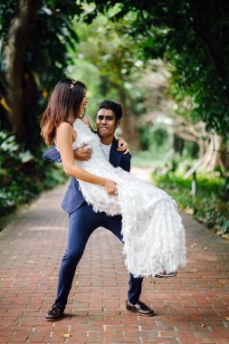 Nişanlı bir ırklararası çift başlattık ve Singapur'da bir parkta düğün fotoğraf çekmek. Bir Hintli taşıyan ve Çin karısı iplik ve her ikisi de glee ve keyfi gülüyorlar.