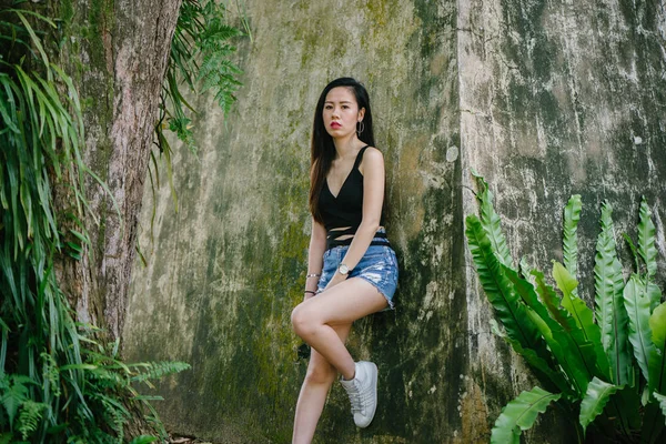 Portrait of a young Asian Chinese woman . She is surrounded by lush, verdant greenery and plants. She is dressed comfortably and stylishly