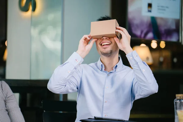 photogenic, young Chinese man tries on Virtual Reality goggles and is smiling and delighted as he tries it for the first time.