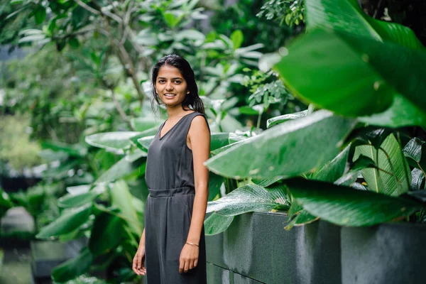 緑豊かな緑の庭に立って若いインド人女性の率直な肖像画 彼女はプロのグレーを着ているスモック ジャンプ スーツと笑顔 — ストック写真