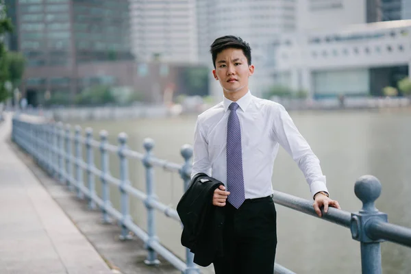 Portrait of Asian man  along the Singapore River in the day. He\'s professionally dressed in a white shirt, tie