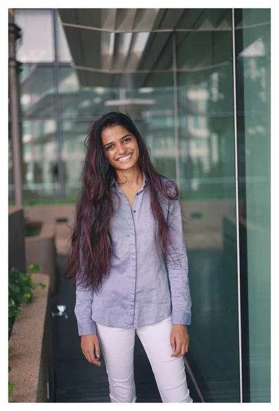 正式な衣服を身に着けているガラスの壁の近くに立って若いインド人女性の肖像画 彼女は何気なく自然な方法でカメラに向かって笑っています — ストック写真