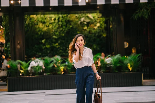 若いシンガポール中国 アジア の女性は 彼女が街を歩いて 彼女の電話で話しています 彼女はよく服を着て 白いシャツにネイビーのパンツにプロ — ストック写真