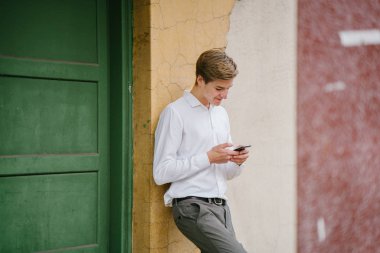 Stüdyo portre gülümseyen genç bir beyaz adam. İş smartphone ile rahat giyiniyor. O genç, yakışıklı, fotojenik ve mutlu, kendine güvenen ve heyecanlı görünüyor.