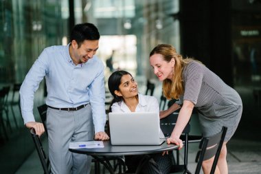 farklı bir takım 3 kişi bir dizüstü bilgisayar etrafında bir tartışma gün açık bir alanda yaşıyorsanız. Gülümse ve konuşmak gibi enerjik ve neşeli vardır.