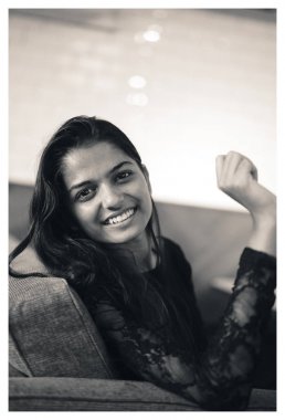 Siyah ve beyaz bir genç ve çekici Hint Asyalı kadın portresi bir kanepede oturuyor. Rahat ve gülümseyen bir kız. Bayan zarif siyah elbise giymiş. Bir kafe ya da office oturuyor.