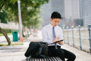 Bir defter Singapur Nehri boyunca onun dolma kalem ile gün içinde yazılı Asya adam portresi. O profesyonel bir beyaz gömlek giymiş, ama onun ceket kravat vardır.