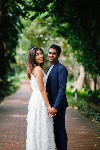 Portrait of interracial couple taking wedding photos in a beautiful park in the day. An Indian man and his Chinese fiance  on a pathway.