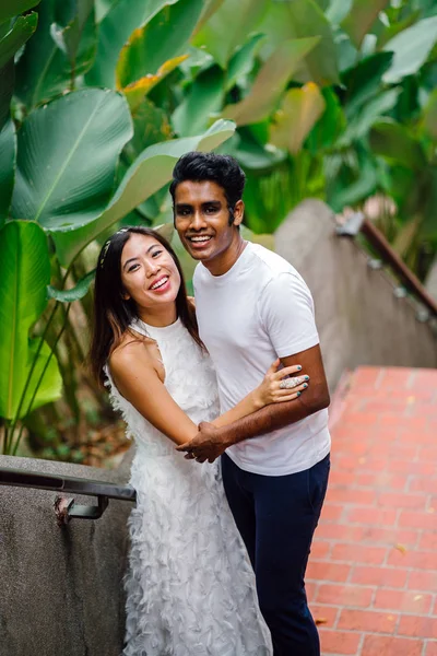 Portrait of young, interracial couple taking photos after getting engaged in Fort Canning, Singapore. They are laughing and playing around; happy and excited about their future.