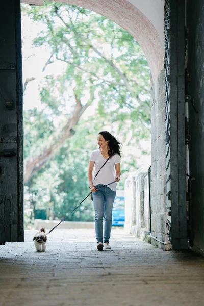 Portrait of a young Pan Asian woman sitting with her young shih tzuh puppy dog in the park in the day. She is smiling and they are both enjoying the warm day.