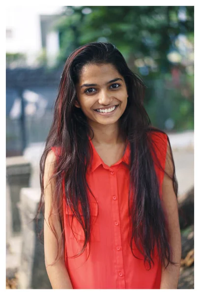 Portrait of a young Indian student  smiling with a campus, university or coworking space in the background. She\'s wearing an orange blouse