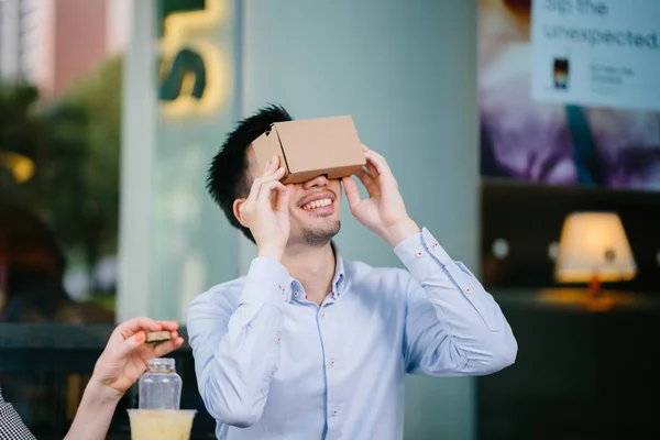 photogenic, young Chinese man tries on Virtual Reality goggles and is smiling and delighted as he tries it for the first time.