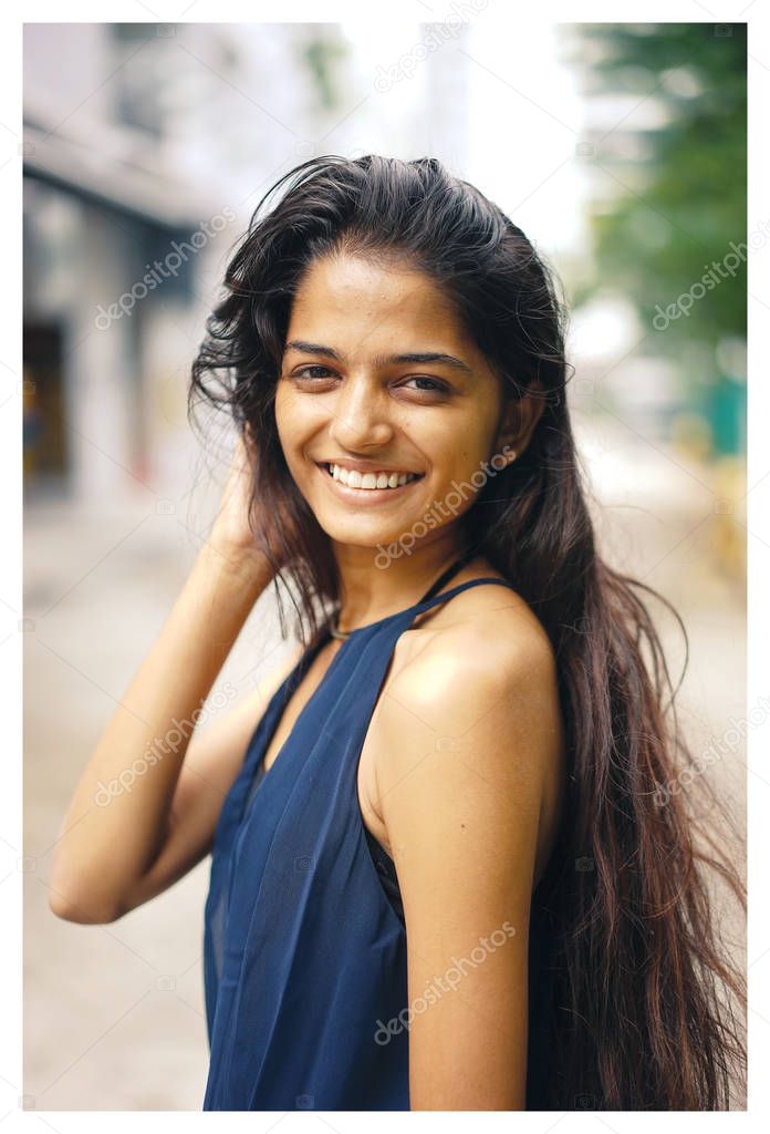 A young and attractive Indian woman in an elegant blue dress walks on the street in the city. She's smiling in the day.