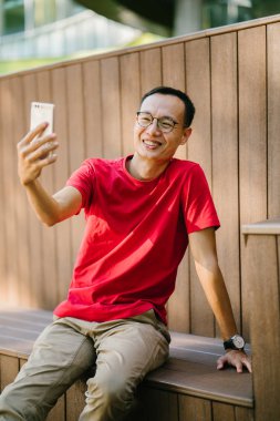 bir parkta onun telefonda konuşan orta yaşlı Asya adam. O gün batımında telefonundan türleri gibi gülümser ve ahşap bir yapı üzerinde oturuyor. O rahat bir tişört ve gevşek pantolon giymiş.