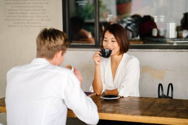 Çinli Asyalı kadın kahve ile genç bir beyaz adam yaşıyor. Onlar rahat bir kafe ya da uzay coworking gün içinde yetişmeye ve onlar rahat konuşmak gibi gülümseyen.