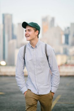 dikey bir genç ve çekici beyaz beyaz adam (turist veya öğrenci) oturma ve gündoğumu veya günbatımı Asya beton bir araba parkta gülüp. O gülümsüyor ve rahat.