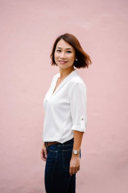 Stüdyo düz pembe arka plan karşı bir Çinli Asyalı kadın portresi. O zarif bir beyaz bluz ve kot pantolon (casual akıllı) bir bob ile giyinmiş ve o (uçan saç kamçı gibi gülümsüyor)