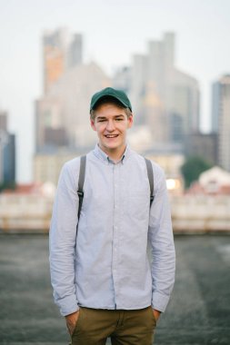 dikey bir genç ve çekici beyaz beyaz adam (turist veya öğrenci) oturma ve gündoğumu veya günbatımı Asya beton bir araba parkta gülüp. O gülümsüyor ve rahat.