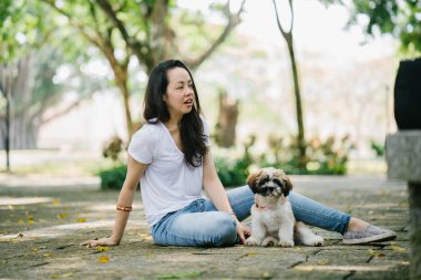 Onun genç shih tzuh yavru köpek park ile gün içinde oturan genç Pan Asya kadın portresi. Gülümsüyor ve her ikisi de sıcak gün tadını çıkarıyor.