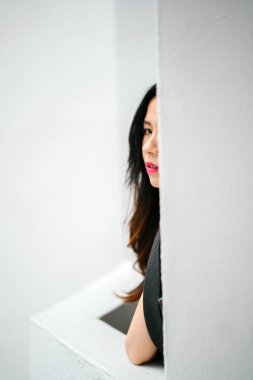 Genç Çin Asya modeli bir beyaz duvar ayağı arkasından bakan ve yoğun kameraya bakan. Çok şık ve zarif giyimli kız.