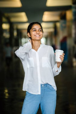 Ayakta günde bir fincan kahve tutan bir kafe (kahve dükkanı) dışında bir gülümseyen genç, Hint Asyalı kadın portresi.