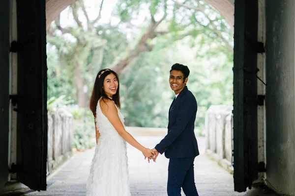 印度新郎抱着他的中国妻子的妻子和并排站在公园里 这对异族情侣在白天的拱门下拍照留念 并微笑着 — 图库照片
