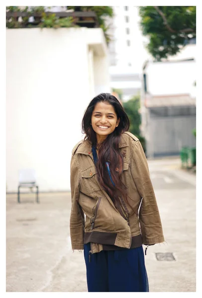 A young and attractive Indian woman in jacket on the street in the city. She\'s smiling in the day.