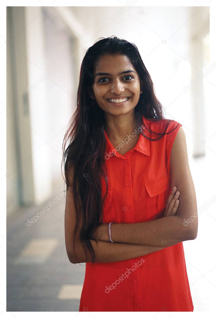 Portrait of a young Indian student  smiling with a campus, university or coworking space in the background. She's wearing an orange blouse 