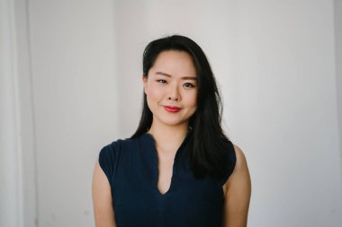 Düz beyaz arka plan karşı genç bir Asyalı kadın portre kafa vurdu. O Lacivert bir elbise giyiyor ve şık ve zarif giyindi ve Görüntüleyici gülümsüyor.