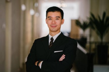 Kameraya gülümseyen yakışıklı, kendinden emin ve genç Asyalı bir adam portresi. O bir koyu takım elbise, beyaz gömlek, profesyonel kravat ve cep Meydanı..