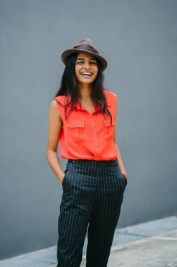 Bir genç, çekici Hint Asya portresi öğrenci moda. O gülümseyen ve güneşin düz gri mavi arka plan karşı ayakta.