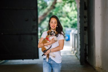 Onun köpeği ve yeşil bir parkta kamera için sıcak bir günde parkta gülümseyen genç bir Pan Asya kadın portresi. Köpek oyuncak doğurmak shih tzuh olduğunu.