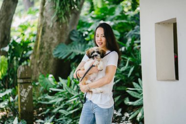Onun köpeği ve yeşil bir parkta kamera için sıcak bir günde parkta gülümseyen genç bir Pan Asya kadın portresi. Köpek oyuncak doğurmak shih tzuh olduğunu.