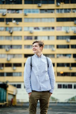 Ayakta ve gülümseyen bir genç çekici beyaz erkek samimi portresi. O arka planda bina bir sarı ile şehirde ve raslantı henüz akıllıca giyindi.