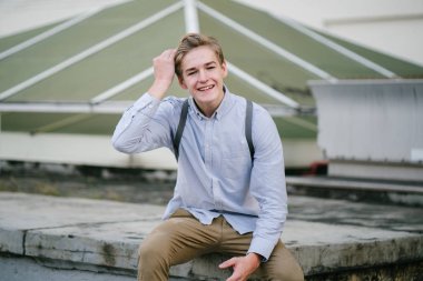 dikey bir genç ve çekici beyaz beyaz adam (turist veya öğrenci) oturma ve gündoğumu veya günbatımı Asya beton bir araba parkta gülüp. O gülümsüyor ve rahat.