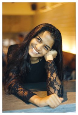 Bir çekici ve genç Hintli Asyalı bir kafede portresi. O bir zarif siyah dantel elbise ve doğal olarak gülümseyen.