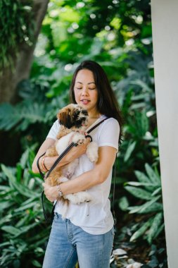 Onun köpeği ve yeşil bir parkta kamera için sıcak bir günde parkta gülümseyen genç bir Pan Asya kadın portresi. Köpek oyuncak doğurmak shih tzuh olduğunu.