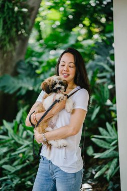 Onun köpeği ve yeşil bir parkta kamera için sıcak bir günde parkta gülümseyen genç bir Pan Asya kadın portresi. Köpek oyuncak doğurmak shih tzuh olduğunu.
