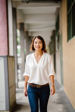 Singapur, Asya bir koridor boyunca genç Çinli Asyalı kadın yürüyor. O akıllıca iş casual giyinen, saç kısa kesilmiş ve o koridorda elini kolunu sallaya dönüyor gibi gülümsüyor.