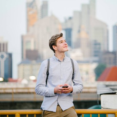 Açık havada duran genç çekici beyaz erkek portresi akıllıca telefon ile şehirde giyinmiş.