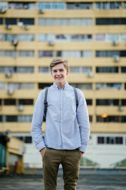 Ayakta ve gülümseyen bir genç çekici beyaz erkek samimi portresi. O arka planda bina bir sarı ile şehirde ve raslantı henüz akıllıca giyindi.