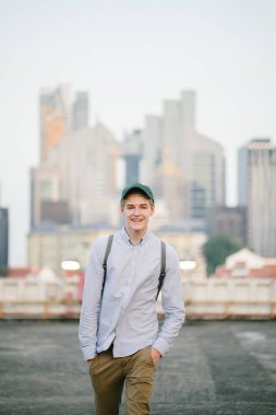 dikey bir genç ve çekici beyaz beyaz adam (turist veya öğrenci) oturma ve gündoğumu veya günbatımı Asya beton bir araba parkta gülüp. O gülümsüyor ve rahat.