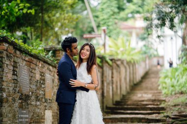 ırklararası çift (Hintli adam, Çinli kadın) günde bir parkta düğün fotoğraf için poz vermek. Eski taş merdiven üstünde olduklarını ve ve gülümseyen ve fotoğraf çekmek gibi gülüyor.